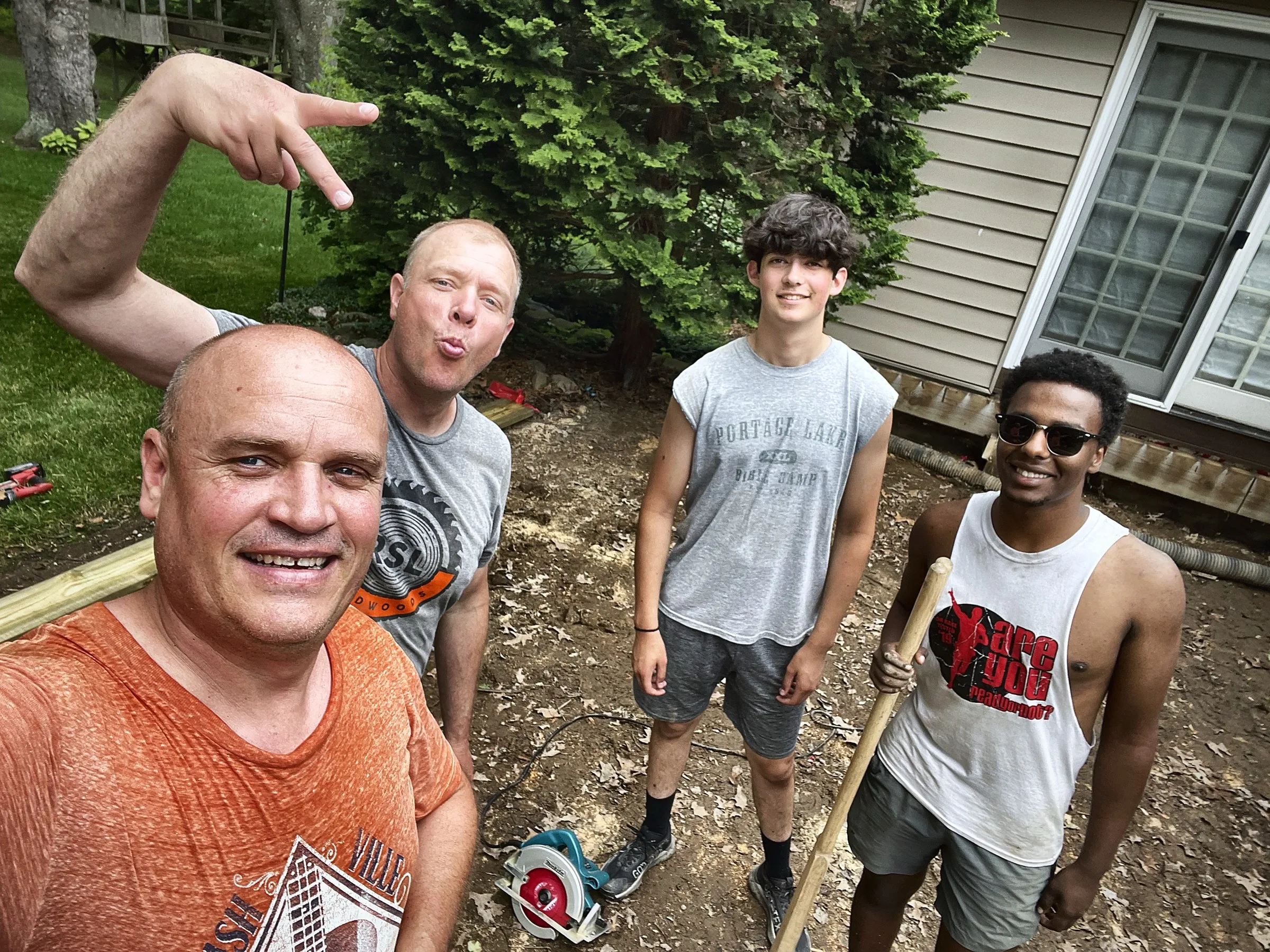 The crew grinning in a jobsite selfie with a circular saw and fresh lumber on the ground