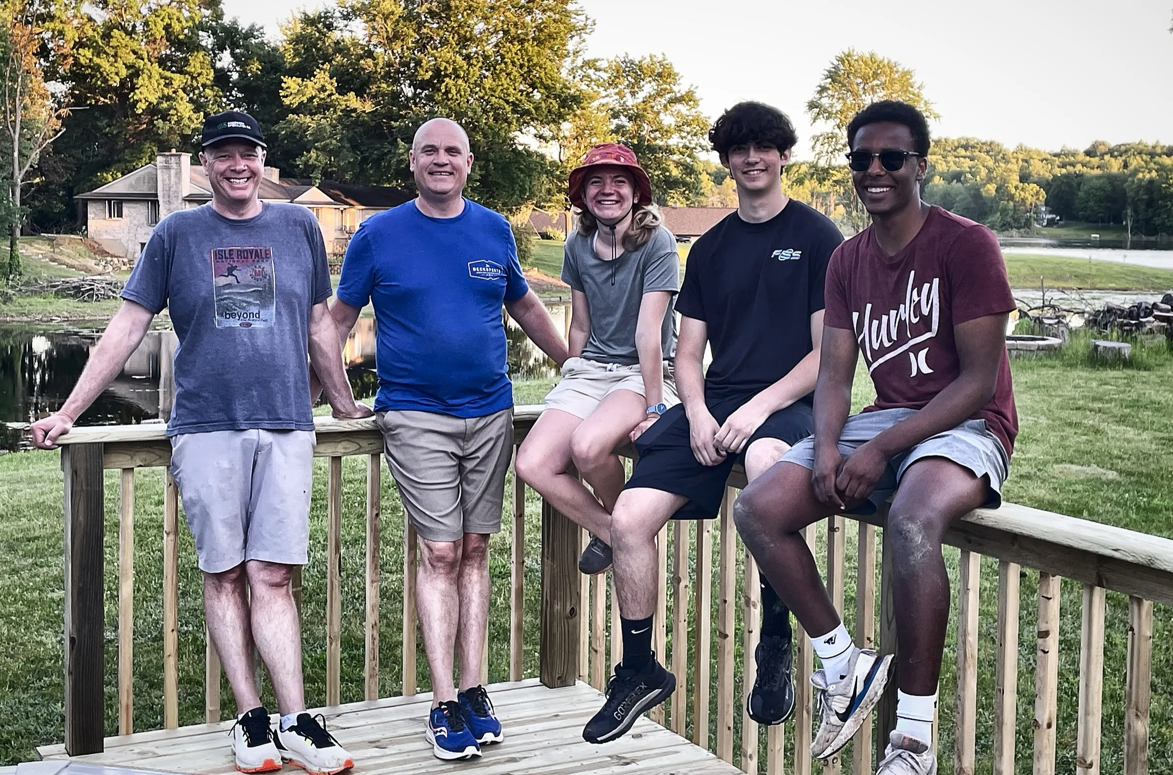 The crew of five relaxing on a new wood deck railing by a pond at golden hour