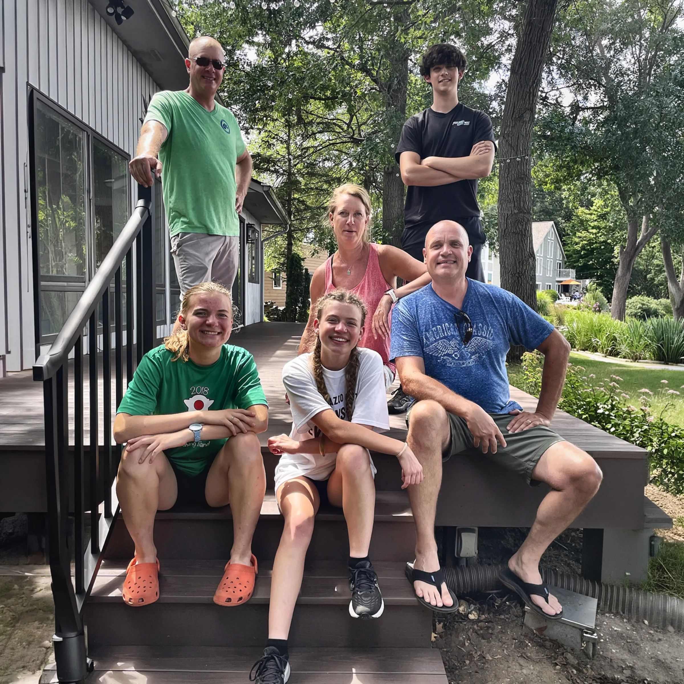 A smiling customer family of six sitting on the steps of their brand-new deck