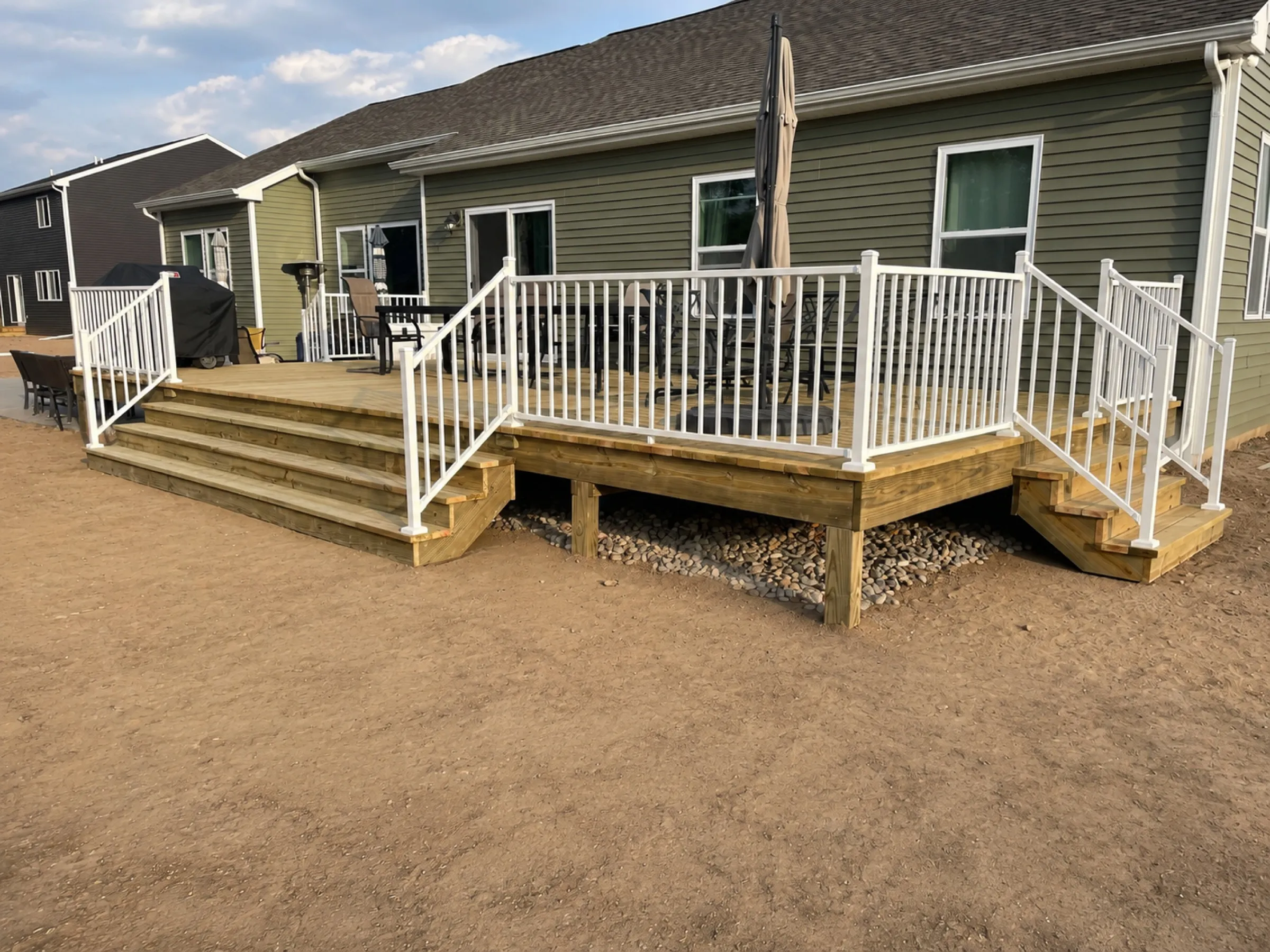 New treated wood deck with white aluminum railing and two corner staircases on a green ranch home